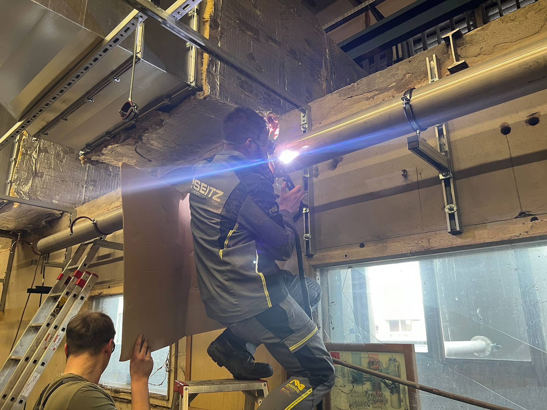 Techniker schweißt Rohrleitung unter Decke in Industriehalle