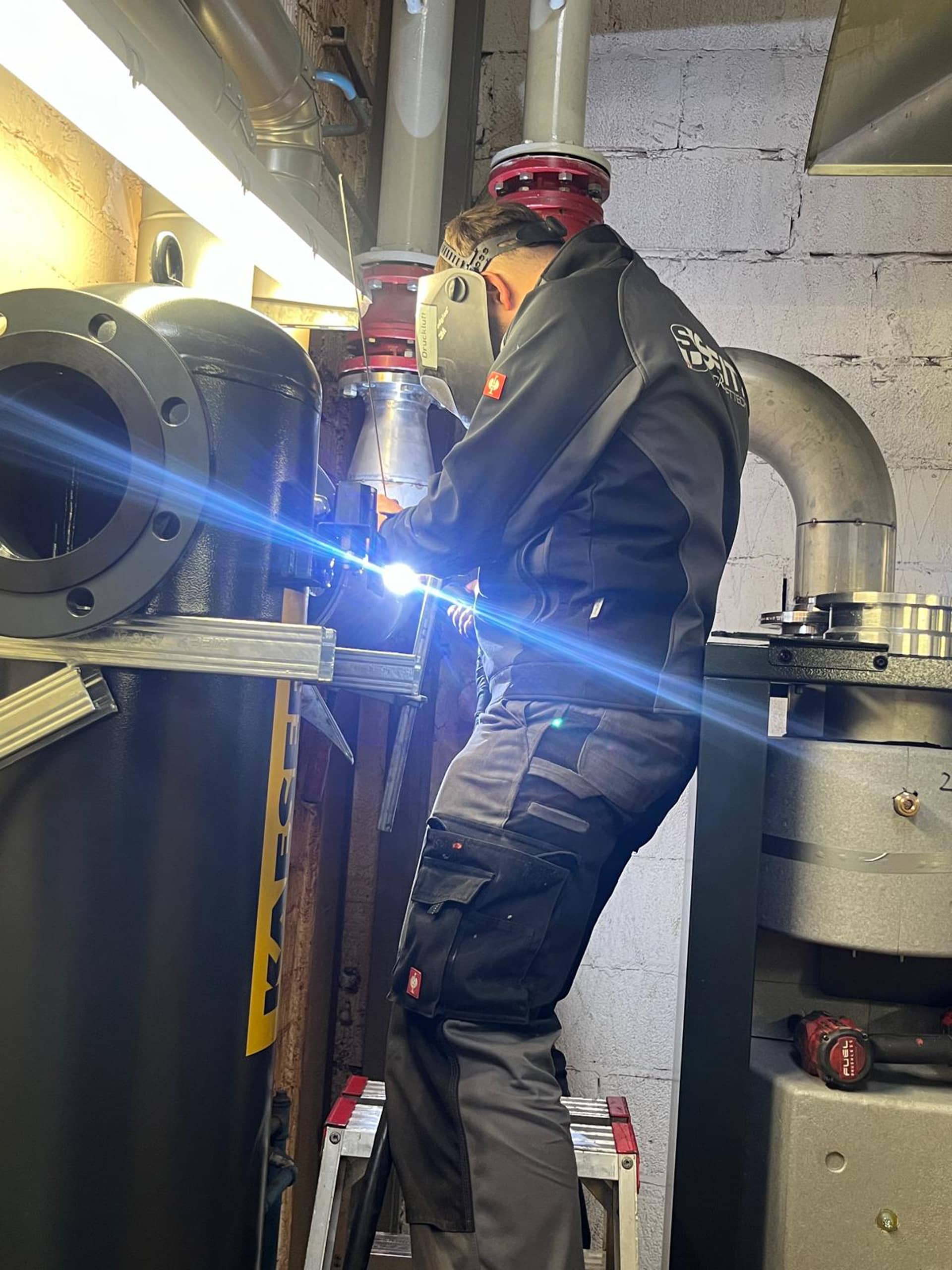 Techniker schweißt Rohrleitung unter Decke in Industriehalle