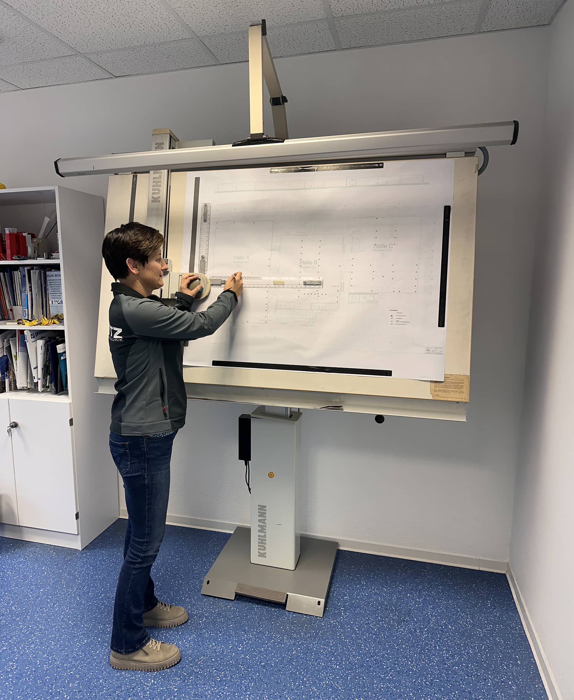 Frau arbeitet an großem technischen Zeichenbrett im Büro